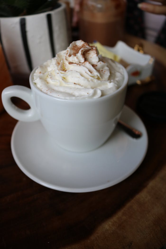 creative-02 Whipped cream topped cappuccino in a white cup on a wooden table, perfect for cozy moments.